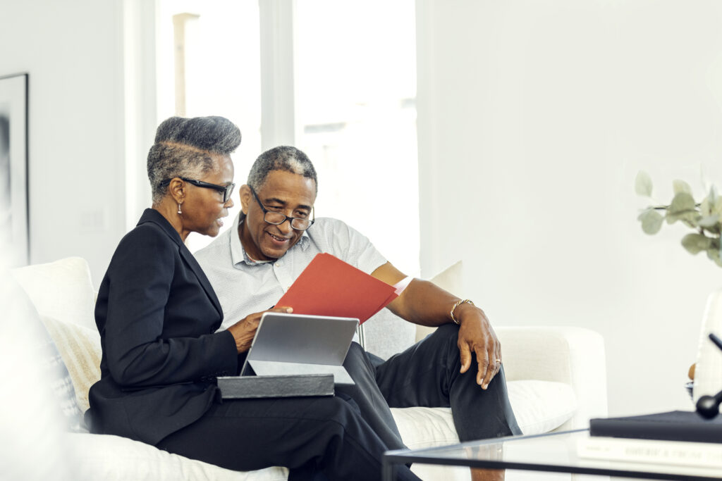 Two mature adults sitting on couch both looking over financial documents with smiles on their faces