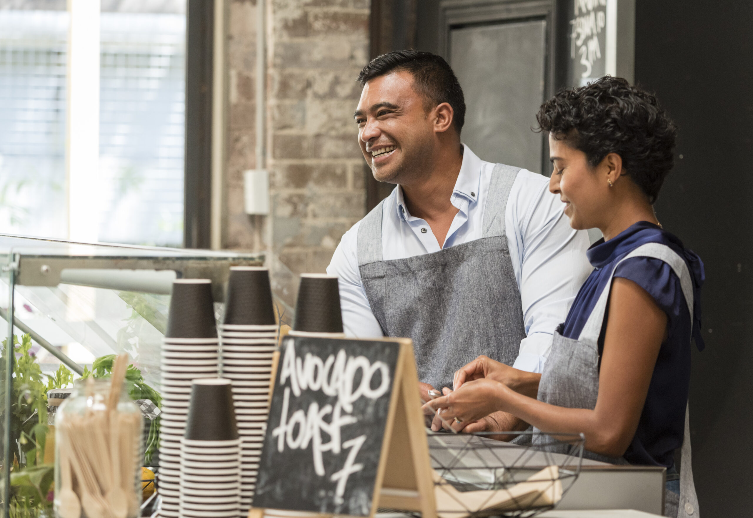 Two smiling restaurant workers behind the counter serving coffee