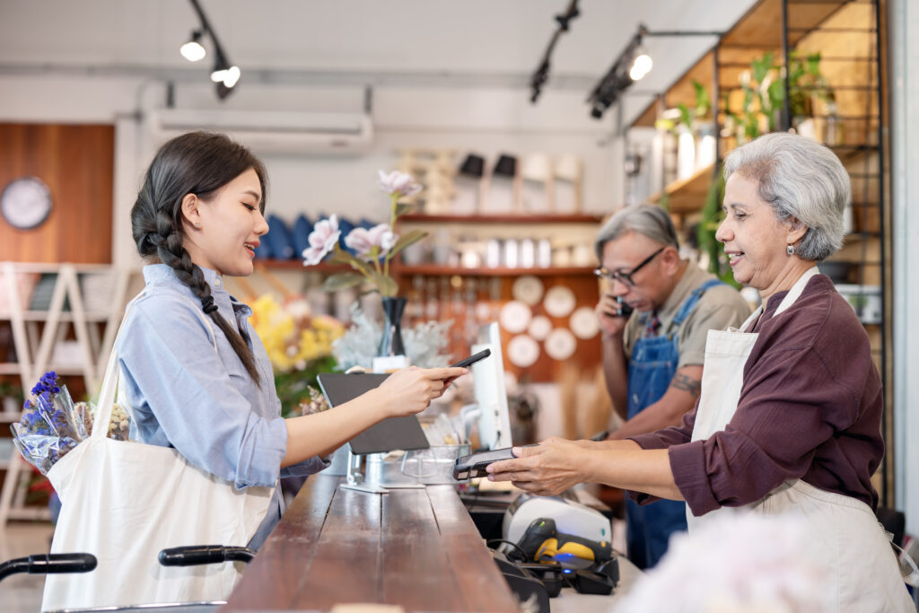 A customer paying with a phone at retail counter where two employees are working behind the counter with their storefront in the background