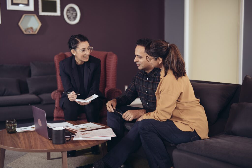 Financial consultation in the office with three people one financial consultant speaking to a couple over a coffee table with laptop and papers on it