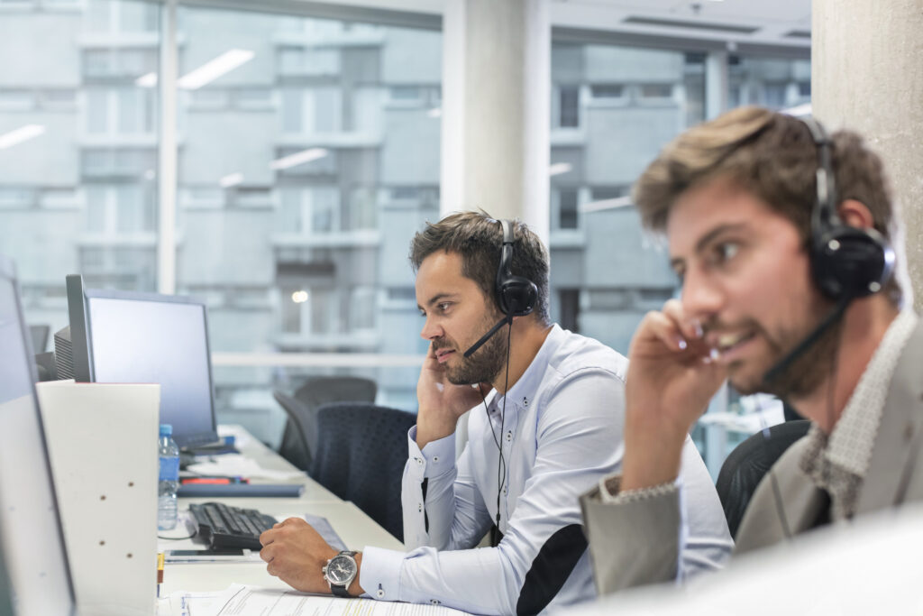 Two financiers talking on headsets while working at computers