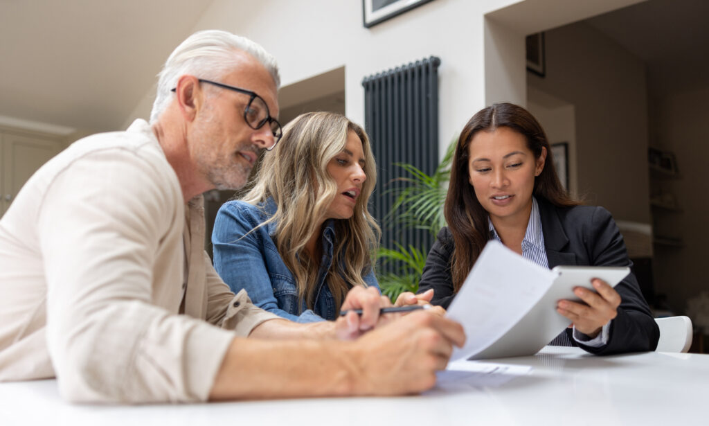 Three people sitting at a desk looking over paperwork. The person on the right is holding the paper explaining something to the other two.