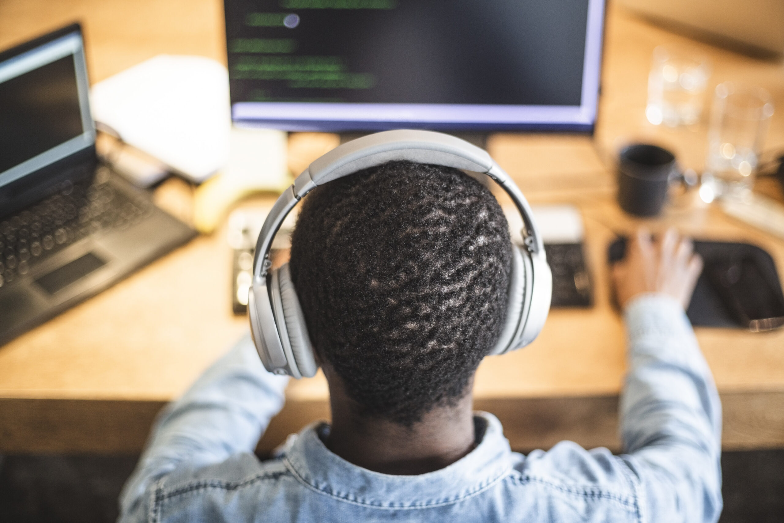 Rear view of someone wearing headphones and working at a desktop computer