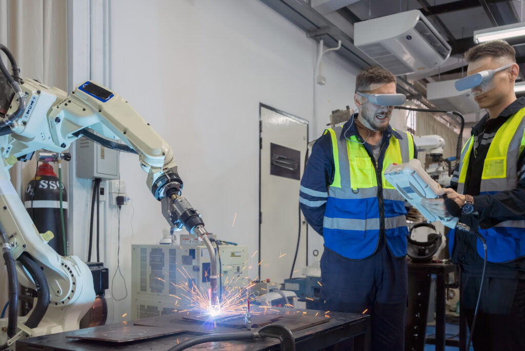 Two engineers pilot a mechanical robotic machine while wearing visors and safety vests