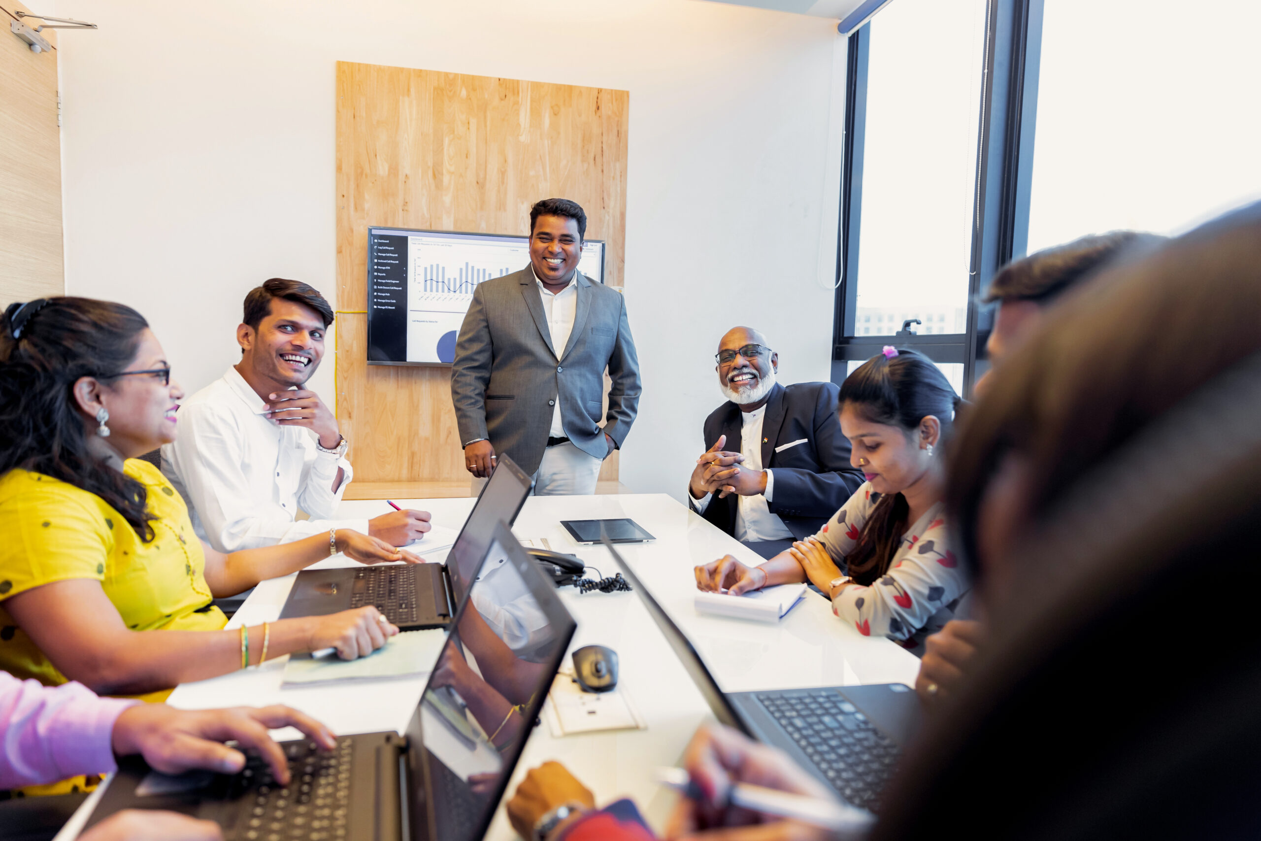 Staff attending a meeting in the board room smiling with laptops open